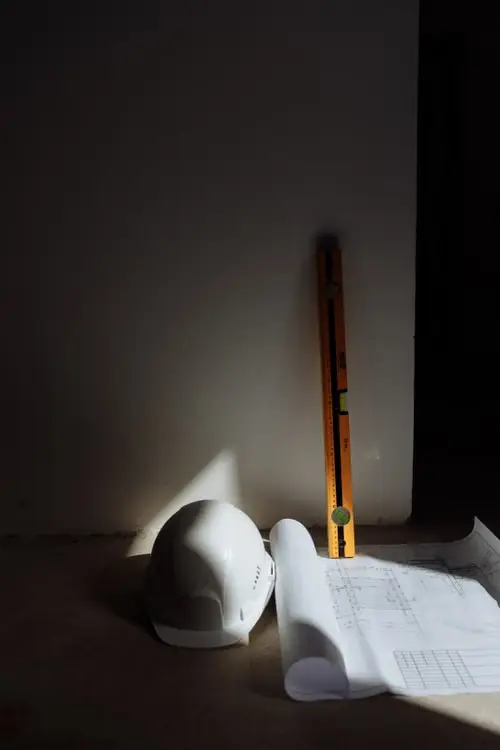 Casque de chantier blanc et niveau à bulle sur des plans d'architecte imprimés pour une demande de permis de bâtir.