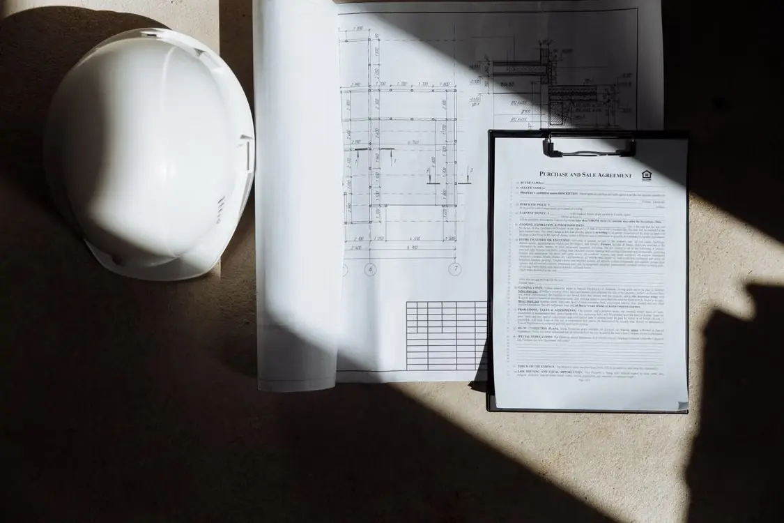 Vue de dessus d'un casque de chantier blanc, d'un plan d'architecte détaillé et d'un dossier administratif pour une demande de permis de bâtir.